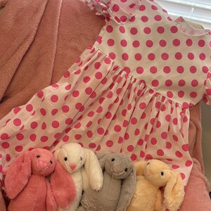 Op de afbeelding: Vier pluche konijnen speelgoed in roze, wit, grijs en geel. De konijnen zitten op een roze en wit gepolka-dotte jurk.