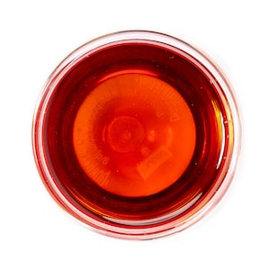 Op de afbeelding: Een glazen kom gevuld met een donkerrode vloeistof. De vloeistof heeft een lichte oranje tint en een label op de bodem met de tekst "Desco Products, Inc.  Made in USA  8 oz/236 ml".