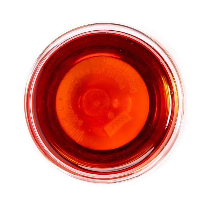 Op de afbeelding: Een glazen kom gevuld met een donkerrode vloeistof. De vloeistof heeft een lichte oranje tint en een label op de bodem met de tekst "Desco Products, Inc.  Made in USA  8 oz/236 ml".