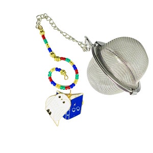 May include: A silver tea infuser with a chain and a charm featuring a white owl and a blue book with glasses. The charm is attached to a colorful beaded chain.
