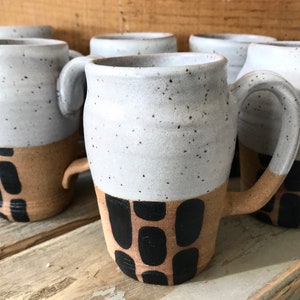 May include: Set of four ceramic mugs with a speckled white glaze and a brown and black geometric design. The mugs have a rounded shape and a handle.