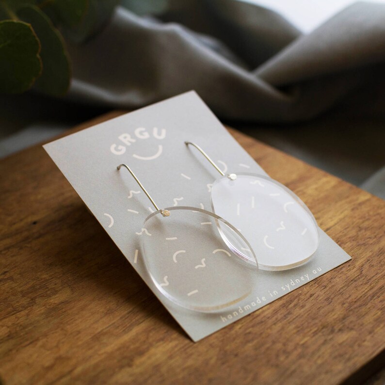 Pode incluir: Um par de brincos de acr&iacute;lico transparente com um design geom&eacute;trico. Os brincos est&atilde;o em um cart&atilde;o com o texto "GRGU handmade in sydney au".