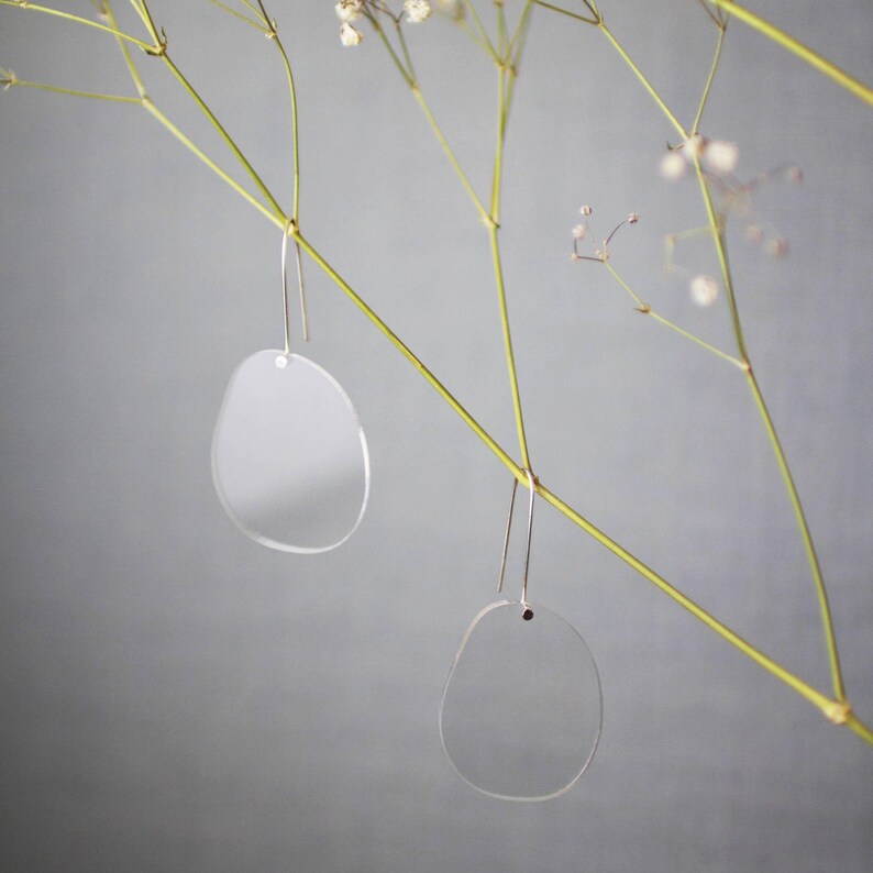Pode incluir: Um par de brincos de acr&iacute;lico transparente com uma forma arredondada e org&acirc;nica. Os brincos est&atilde;o pendurados em um fio fino de prata.