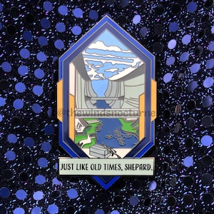 以下が含まれることがあります： 風景画と「JUST LIKE OLD TIMES, SHEPARD」の文字が入った青、金、白のエナメルピン。 ピンは幾何学的な形で、川と空の詳細なイラストが描かれています。