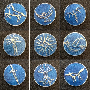 Puede incluir: Nueve pines de esmalte azul con contornos plateados, cada uno con un símbolo diferente. Los símbolos incluyen un caballo, un búho, un dragón, un árbol, una espada, un sol, un barco, un lobo y una serpiente.