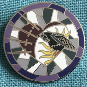 May include: Round enamel pin featuring a raven perched on a sunburst design within a stained-glass style circle. The raven is black and gray, with a heart pierced by swords in the center. The pin has a silver border and a color palette of purple, white, gray, and brown.