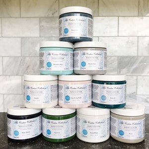 May include: A pyramid of ten paint jars in various colours, including teal, green, white, black, and pink. Each jar has a label that reads "The Couture Collection Paint Couture".