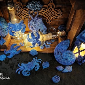 May include: A collection of blue and white ceramic sea life ornaments, including a crab, starfish, nautilus shell, and a bottle with a cork stopper. The ornaments are arranged in a wooden crate with a lantern and a wooden knot design.