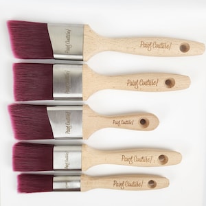 Pu&ograve; includere: Cinque pennelli angolari con setole bordeaux e ferrule argentate. I manici in legno sono etichettati "Paint Couture".