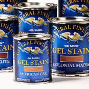 May include: A collection of six cans of General Finishes Gel Stain in various wood tones, including Candlelite, American Oak, Colonial Maple, and Java. The cans are blue with gold accents and feature the General Finishes logo.