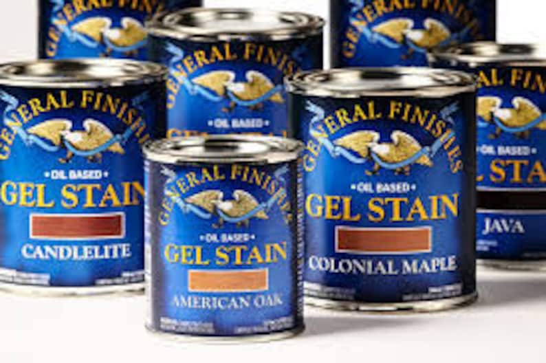 May include: A collection of six cans of General Finishes Gel Stain in various wood tones, including Candlelite, American Oak, Colonial Maple, and Java. The cans are blue with gold accents and feature the General Finishes logo.