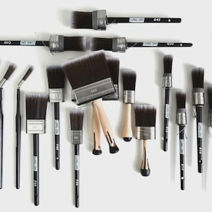 May include: An assortment of paint brushes with black handles and dark bristles. Some brushes have angled heads, while others are flat. The handles have the text "CLING ON" printed on them. The brushes are arranged on a white surface.