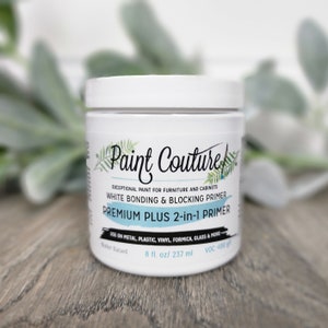 May include: White Paint Couture Premium Plus 2-in-1 Primer in a white jar with a black label. The label says "Exceptional paint for furniture and cabinets. White Bonding & Blocking Primer. Premium Plus 2-in-1 Primer. Use on metal, plastic, vinyl, formica, glass & more. Water Based. 8 fl. oz/ 237 ml. VOC 100 g/l."