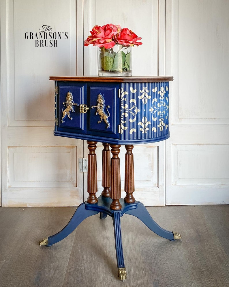 May include: A blue and brown side table with gold lion accents and a white and gold patterned design. The table has a rounded top and four legs. The table is decorated with a vase of red roses.