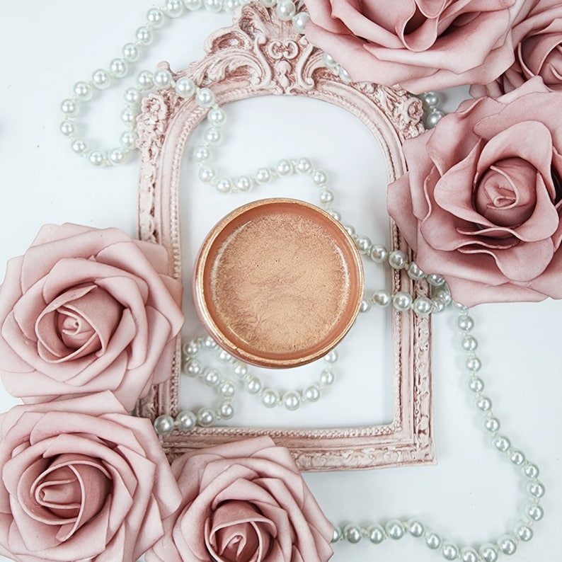 May include: A gold-colored metal trinket dish with a pearl necklace draped around it. The dish is surrounded by several blush-colored silk roses.