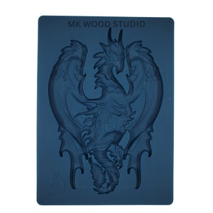 May include: A dark blue silicone mold featuring a detailed dragon design with outstretched wings. The mold has the text "MK WOOD STUDIO" at the top and a circular logo with the text "Zari" at the bottom. The dragon is the central focus.