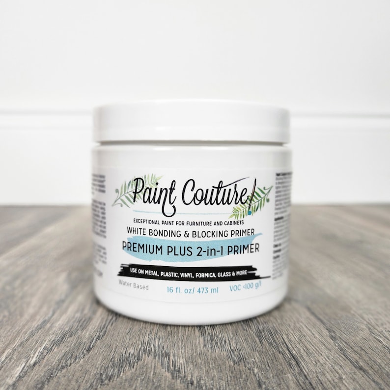 May include: A white jar of Paint Couture Premium Plus 2-in-1 Primer. The jar is labelled "Exceptional Paint for Furniture and Cabinets" and "White Bonding & Blocking Primer". The jar is 16 fluid ounces and contains 473 millilitres. The jar is water-based and has a low VOC content.