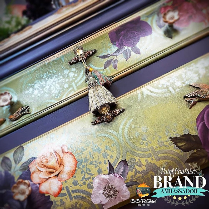 May include: A dresser with a floral design and gold accents. The dresser has three drawers with decorative pulls. The top drawer has a tassel pull. The dresser is painted in a green and gold colour scheme. The text "Paint Couture Brand Ambassador" is visible on the dresser.
