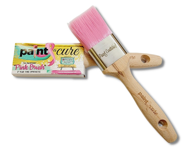 May include: A pink paint brush with a wooden handle and a silver ferrule. The brush is labelled "Paint Couture!" and "paint cure". The packaging for the brush is also visible and says "The Painters "Pink Brush" 2" Flat Fine Synthetic".