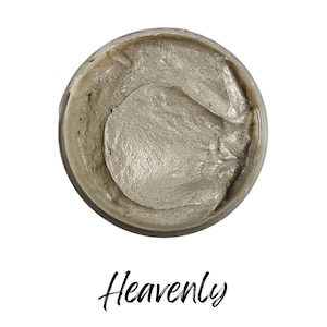 May include: A jar of light gray cosmetic product with a shimmering, textured surface. The word "Heavenly" is written in cursive script below the jar. The product appears to be a facial mask or cream.