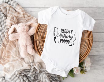 Könnte beinhalten: Weißer Baby-Strampler mit schwarzem Text "Daddy's fishing buddy" und einer schwarzen Silhouette einer Angelrute und eines Fisches.
