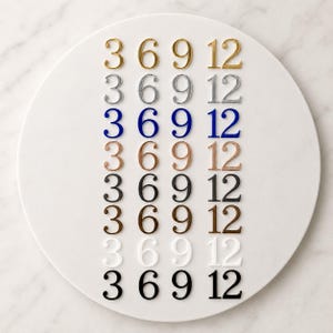 Può includere: Una collezione di numeri metallici disposti in file di 3, 6, 9 e 12. I numeri sono in vari colori, tra cui oro, argento, blu, rame, nero, marrone, bianco e nero. I numeri sono posti su una superficie circolare bianca.