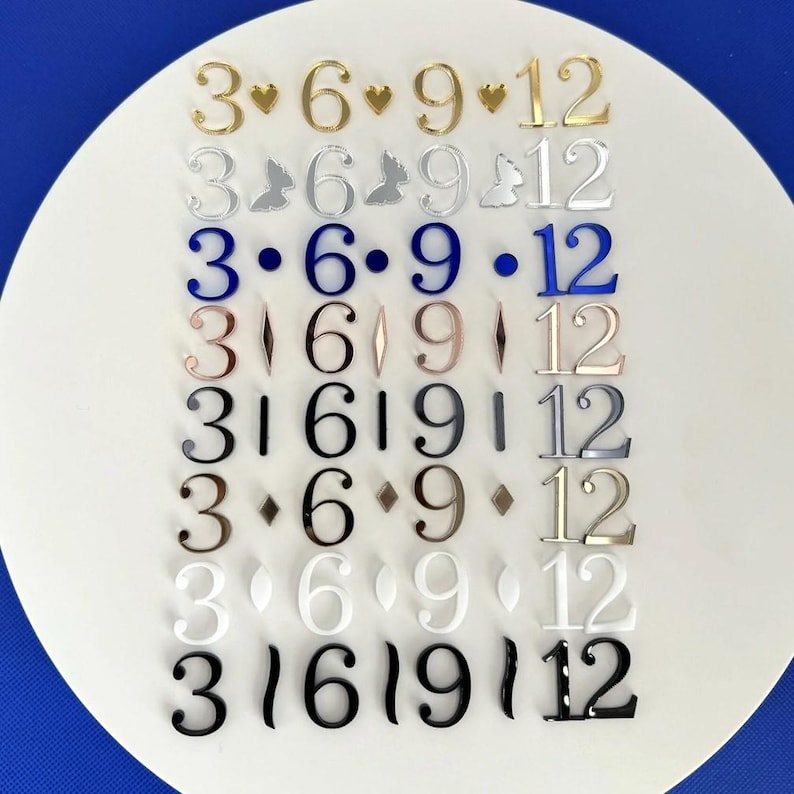 Peut inclure: Une collection de chiffres d&eacute;coratifs de diff&eacute;rentes couleurs et styles, dispos&eacute;s sur une surface blanche. Les chiffres incluent 3, 6, 9 et 12, certains comportant des ornements comme des c&oelig;urs et des diamants. Les chiffres sont en or, argent, bleu et autres couleurs.