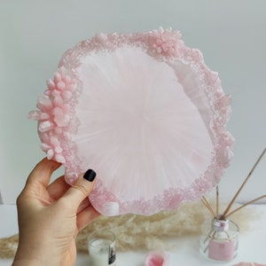 May include: A light pink resin tray with a decorative edge featuring crystal and floral accents. The tray is round with a smooth center and a textured border. The tray is approximately 8 inches in diameter.