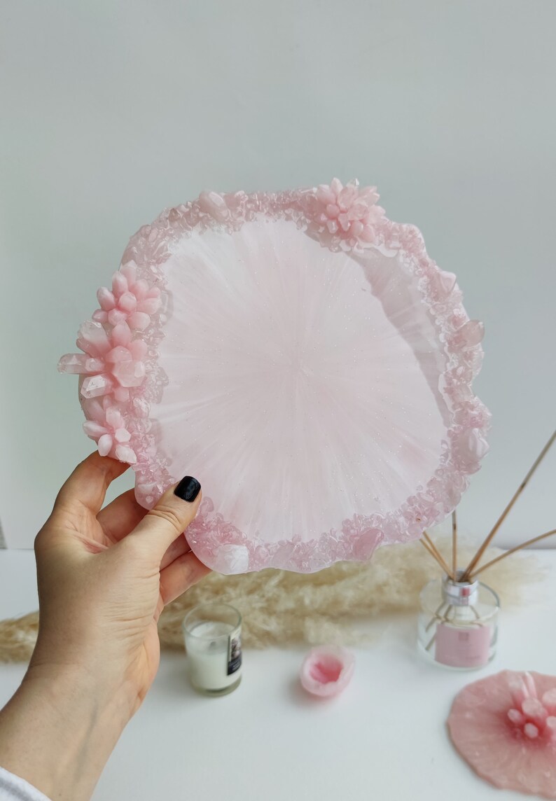 May include: A light pink resin tray with a decorative edge featuring crystal and floral accents. The tray is round with a smooth center and a textured border. The tray is approximately 8 inches in diameter.