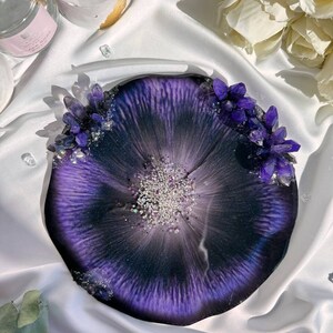 May include: A round, resin tray with a deep purple and black design, accented with silver glitter and clusters of purple crystals. The tray has a unique, organic shape and a glossy finish, perfect for home decor.