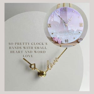 May include: A white and purple clock with gold hands and Roman numeral markings. The clock face has a white and gray textured design. The hands are shaped like a heart and the word "love".