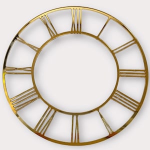 Può includere: Un quadrante dorato con numeri romani. La cornice circolare è realizzata in un materiale metallico lucido. I numeri sono uniformemente distanziati attorno al cerchio interno, creando un design classico ed elegante. Il quadrante è un elemento decorativo.