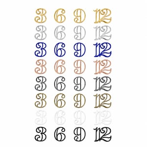 Puede incluir: Una colección de números decorativos en varios acabados metálicos, incluyendo oro, plata, azul y bronce. Los números 3, 6, 9 y 12 se muestran en una fuente cursiva. Los números están dispuestos en filas y columnas sobre un fondo blanco.