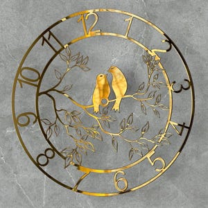 Può includere: Un orologio da parete circolare color oro con un design ispirato alla natura. L'orologio presenta una coppia di uccelli appollaiati su un ramo con foglie, circondati dai numeri da 1 a 12. L'orologio è in metallo e ha un'estetica moderna.