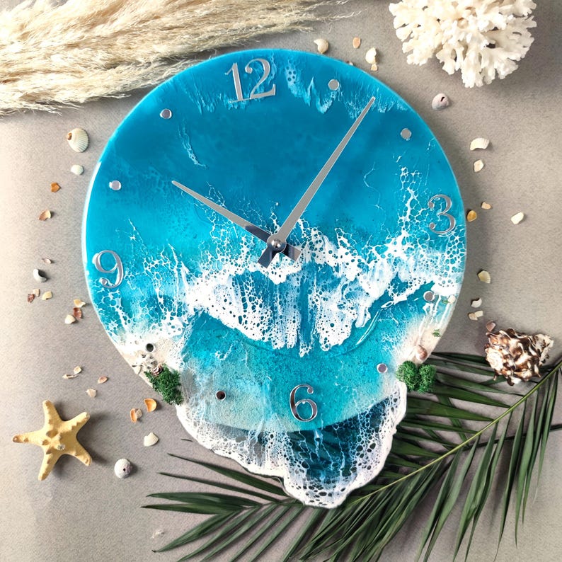 Peut inclure: Une horloge murale ronde avec un motif de vagues oc&eacute;aniques bleues. Le cadran de l'horloge pr&eacute;sente des chiffres et des aiguilles argent&eacute;s, avec un motif de vagues blanches &eacute;cumeuses. L'horloge est d&eacute;cor&eacute;e de coquillages et d'une &eacute;toile de mer.