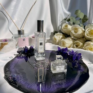 May include: A decorative tray with a deep purple and black resin finish, adorned with purple crystals and small perfume bottles. A Jo Malone perfume bottle and a Miss Dior perfume bottle are displayed on the tray.