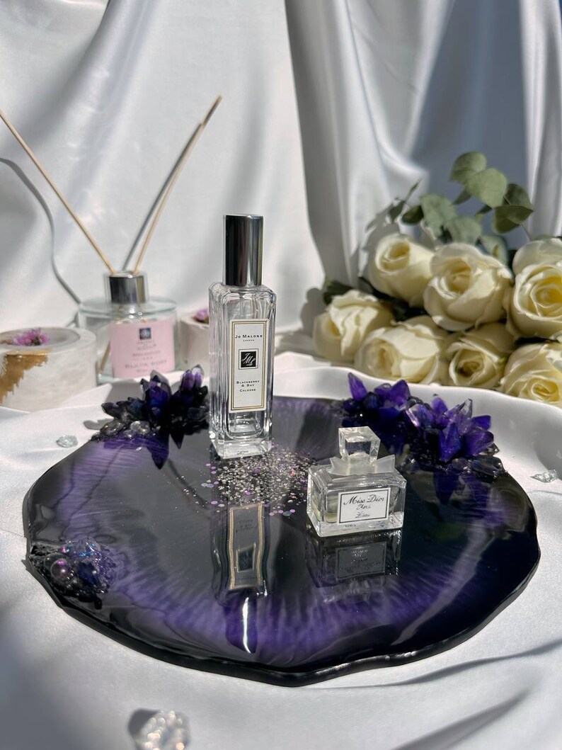 May include: A decorative tray with a deep purple and black resin finish, adorned with purple crystals and small perfume bottles. A Jo Malone perfume bottle and a Miss Dior perfume bottle are displayed on the tray.