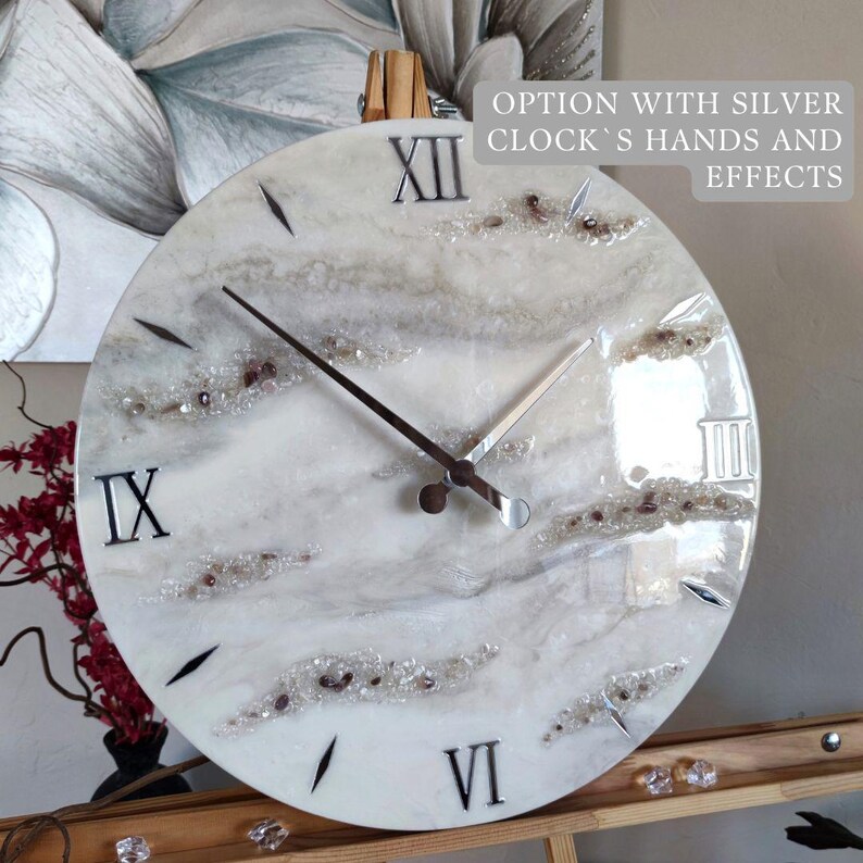 May include: A round wall clock with a white and gray marbled design. The clock features black Roman numerals, black hands, and decorative crystals. The text "OPTION WITH SILVER CLOCK'S HANDS AND EFFECTS" is visible.