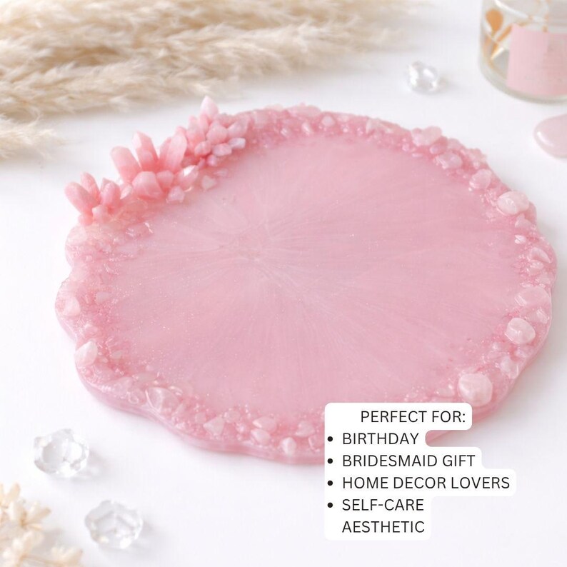May include: A pink resin tray with a textured, crystal-like border. The tray has a smooth, glossy surface and is decorated with small, light pink crystals. The tray is round with an irregular edge. The text on the image says "PERFECT FOR: BIRTHDAY, BRIDESMAID GIFT, HOME DECOR LOVERS, SELF-CARE, AESTHETIC."