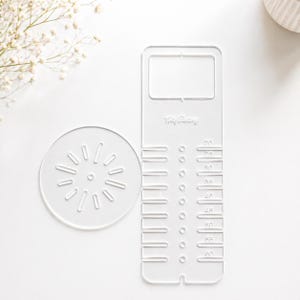 Peut inclure: Outils de décoration de gâteaux en acrylique transparent. Comprend un pochoir rond avec un motif en forme d'éclat de soleil et un outil rectangulaire avec des mesures de 20 à 60. L'outil rectangulaire porte le texte "Way Baking".