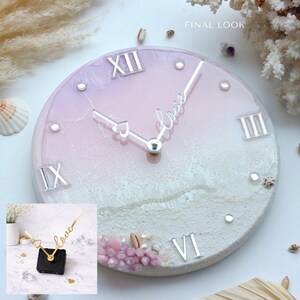 Puede incluir: Un reloj de pared redondo con una esfera degradada rosa y blanca, n&uacute;meros romanos y manecillas plateadas. La palabra "love" est&aacute; escrita en cursiva. El reloj est&aacute; decorado con peque&ntilde;os cristales y conchas marinas. El texto "FINAL LOOK" est&aacute; en la esquina superior derecha.