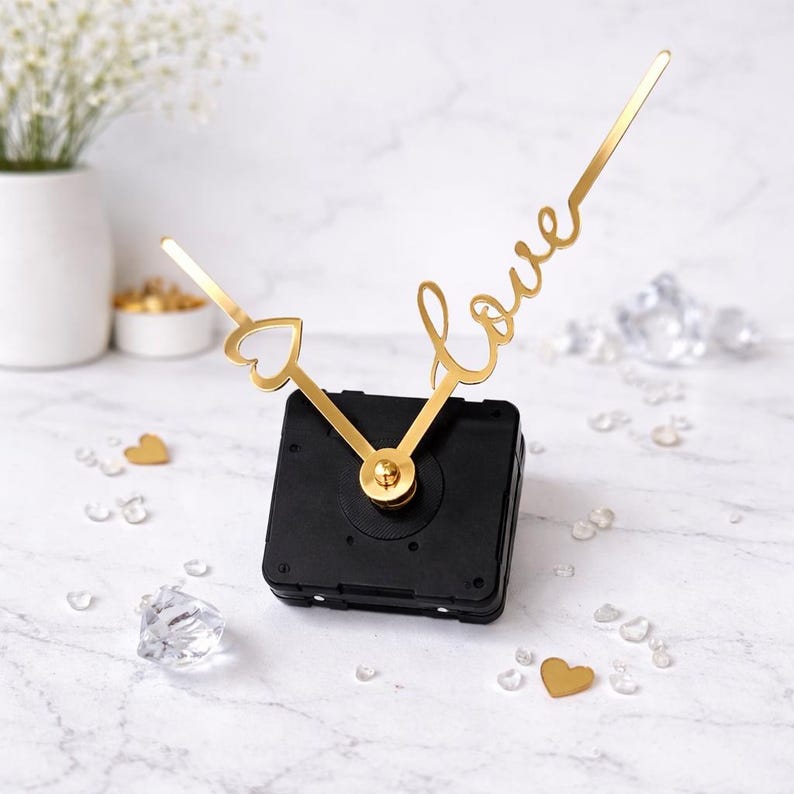 Puede incluir: Mecanismo de reloj negro con manecillas doradas. Una manecilla tiene forma de coraz&oacute;n, la otra deletrea la palabra "love". Cristales decorativos y acentos de coraz&oacute;n dorado rodean el reloj. Las manecillas miden unos 10 cm.