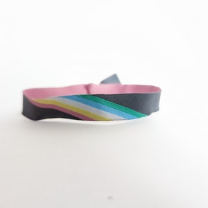 Könnte beinhalten: Ein schwarzes Armband mit einem gestreiften Design in Pink, Gelb, Weiß, Blau und Grün.