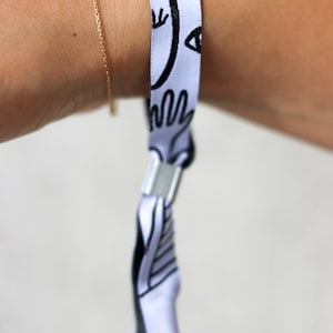 Puede incluir: Pulsera blanca con diseño gráfico en blanco y negro. La pulsera tiene un cierre de broche.