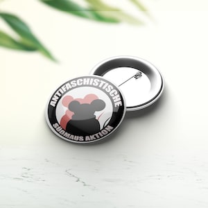 Può includere: Un bottone bianco e nero con una silhouette di topo rossa e il testo "Antifa-schistische Sudmaus Aktion".