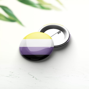 Könnte beinhalten: Ein runder Knopf mit einem gelben, weißen, violetten und schwarzen Streifenmuster. Der Knopf ist an einer silbernen Stecknadel befestigt.