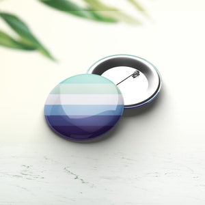 Peut inclure: Un bouton rond avec un design rayé bleu, blanc et vert. Le bouton est attaché à un dos de broche argenté.