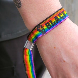 Könnte beinhalten: Ein Regenbogen-Armband mit dem Text "Black Lives Matter" in schwarzen Buchstaben.
