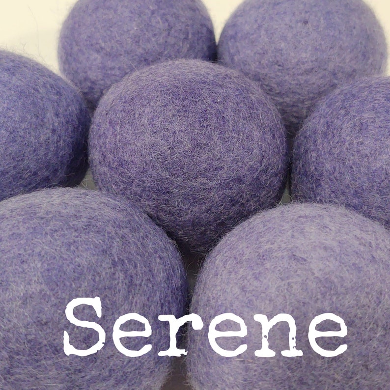 May include: A set of six lavender-colored wool dryer balls. The balls are soft and fluffy, and they are arranged in a circle. The word "Serene" is written in white letters on the bottom of the image.
