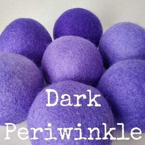 May include: A group of seven dark periwinkle wool dryer balls. The balls are soft and fluffy, and they are a natural way to soften laundry and reduce static.